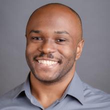 John Michael Clark John Michael Clark wears a grey button-down shirt and smiles in front of a grey background.