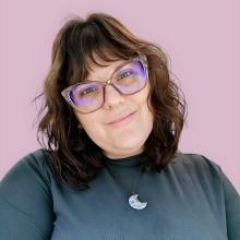 Rebecka Hahnel-Peeters Rebecka Hahnel-Peeters wears a dark turquoise shirt and a blue crescent moon necklace. She smiles with her head tilted to the right in front of a blush pink background.