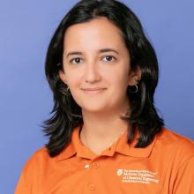 Lea El Khoury Lea El Khoury wears an orange polo with text on the left side of the chest reading "The University of Texas at Austin McKetta Department of Chemical Engineering, Cockrell School of Engineering." She stands in front of a light indigo background.