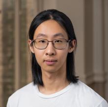 Qing Yao Qing Yao wears a white t-shirt and glasses. He stands in a room with brown wallpaper.