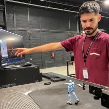 Mauricio Hernández Serrano In a studio, a man in a red shirt stands over a doll with blue legs, which he animates on a computer.