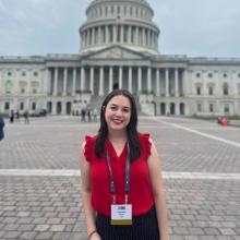 Madison Haiman A woman wears a red blouse and a lanyard and smiles in front of the Texas Capitol building.