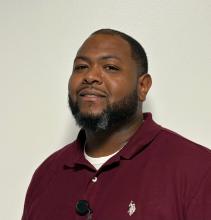 Stedman Holliman A man wears a red shirt and stands in front of a white wall.