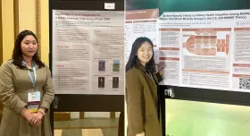 In the first image, a woman with black hair wears a brown dress and blue lanyard in front of a white and orange poster. The title on the poster is "Health Digital Game Adaptation for a Native American Tribe Using Virtual CBPR." In the second image, another woman with long black hair wears a brown jacket and a lanyard, and stands in front of another white and orange poster. The poster reads "Situation-Specific Theory on Kidney Health Inequities Among Midlife Women from Ethnic Minority Groups in the U.S."