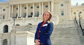 A person in businesswear stands in front of the Texas Capitol building.