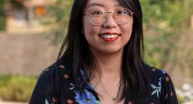A person in a floral blouse and glasses poses for a headshot on campus.
