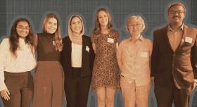 A group of students and their professor stand in front of a grey background.