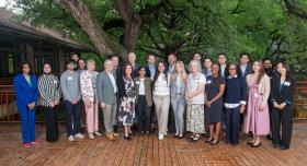A group of researchers wearing business attire and nametags pose for a group photo outdoors.