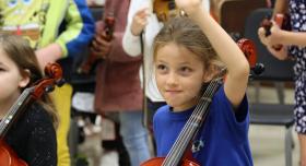 A girl in an elementary school orchestra raises her hand.